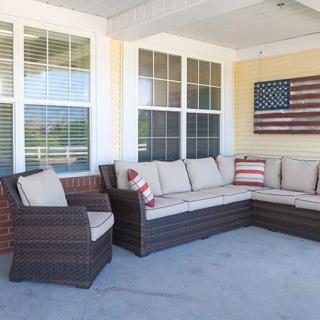 A cozy outdoor patio with wicker furniture, featuring a sectional sofa and armchair adorned with cushions, complemented by flag-themed decor on the wall.