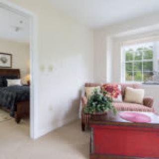 A cozy living area with a view into a bedroom, featuring a couch, table, and large window.