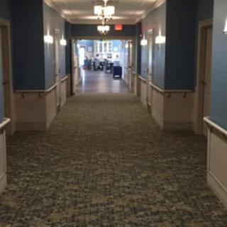 A long hallway with doors on either side, featuring carpeted flooring and overhead lighting.