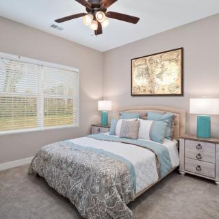A cozy bedroom with a neatly made double bed, accentuated by bedside tables and lamps, featuring wall artwork and a ceiling fan.