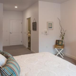 A minimalist bedroom with white walls, featuring a bed and a side table adorned with a vase of branches.