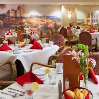 An elegant restaurant dining area with neatly arranged tables, adorned with red napkins and floral centerpieces.