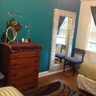 A cozy bedroom featuring a wooden dresser, a tall mirror, and a comfortable chair by the window.