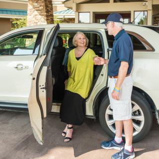 A man assists a senior woman as she exits a car.