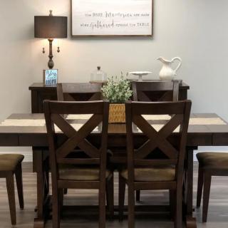 A cozy dining room setup featuring a dark wooden table with matching chairs, a table runner, a decorative plant centerpiece, and a lamp atop a sideboard.