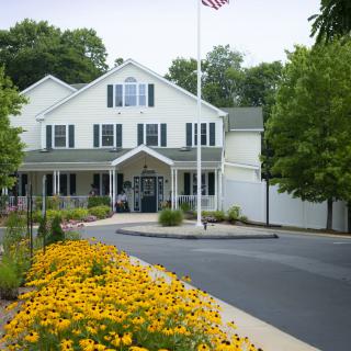 A large white building with a landscaped garden of yellow flowers and an American flag flying on a flagpole at the entrance.