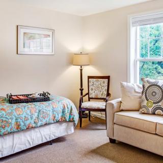 Cozy bedroom with a bed, chair, lamp, and couch near a window.
