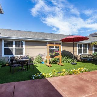 A cozy garden patio with outdoor seating, a swing set, and colorful flowers under a clear blue sky.