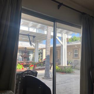 A view of the outdoor patio from behind a sliding glass door, showcasing sunlight and greenery.