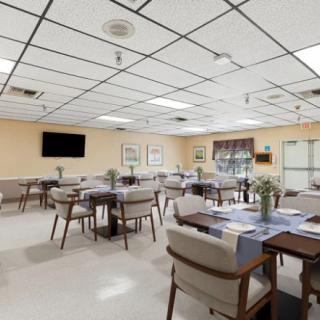Empty dining area with neatly arranged tables and chairs, featuring a television and bright lighting.