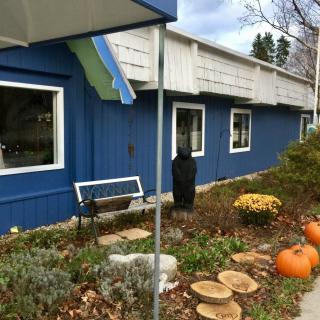 A blue building with autumn-themed outdoor decorations, including pumpkins and a bench among the garden landscape.