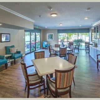 A spacious and bright dining area with multiple tables and chairs, featuring large windows.