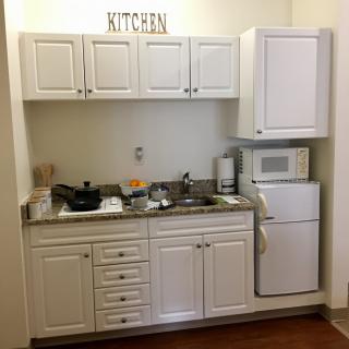 A compact kitchen with white cabinets, a sink, microwave, and small fridge.