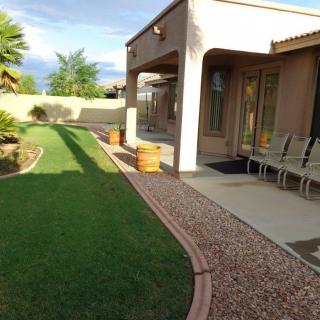 A well-maintained backyard featuring a patio with seating, lush green lawn, and neatly arranged landscaping.