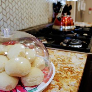 A kitchen with freshly baked bread rolls under a glass dome on the countertop.