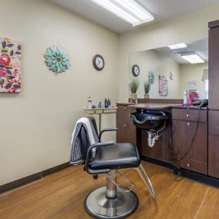 A cozy beauty salon interior featuring a styling chair, mirror, and wall decorations.
