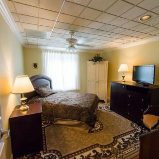 A cozy bedroom with a bed, wardrobe, and a TV, softly lit by lamps.