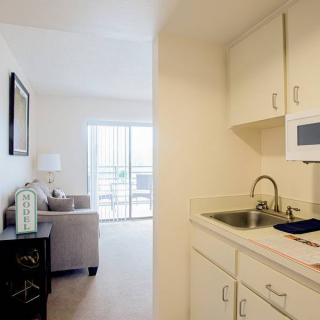 A small kitchen area with white cabinets and a sink, adjacent to a cozy living room with natural light.