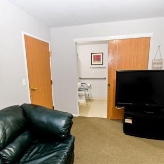 A cozy living room with a leather chair, television, and doors leading to another room.