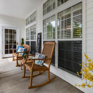 A cozy porch with wooden rocking chairs and decorative pillows, surrounded by large windows and white siding.