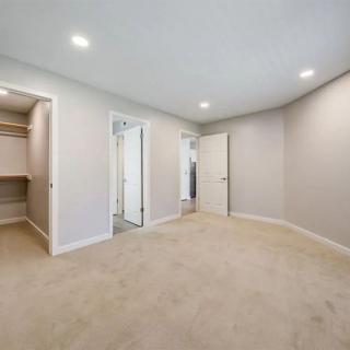 An empty bedroom with a walk-in closet, modern lighting, and neutral-colored carpet flooring.