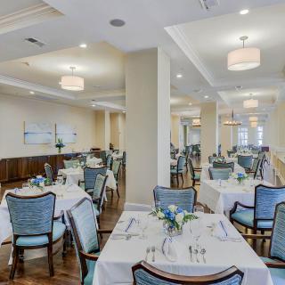 An elegantly set dining room with neatly arranged tables and chairs, featuring soft lighting.