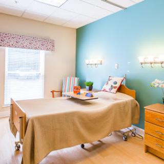 A well-lit hospital patient room featuring a bed, nightstand, and decorative touches for comfort.
