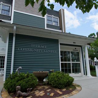 Front entrance of a public library with green siding and surrounding landscaping.