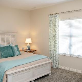 A cozy bedroom with a bed, bedside table, lamp, and large window with curtains.