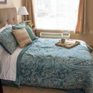 A cozy bedroom with a neatly made bed adorned with patterned bedding and pillows, featuring a warm ambiance.