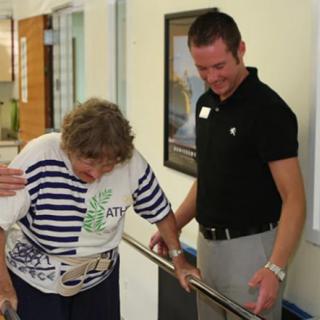An elderly woman receives assistance from a caregiver during a physical therapy session.