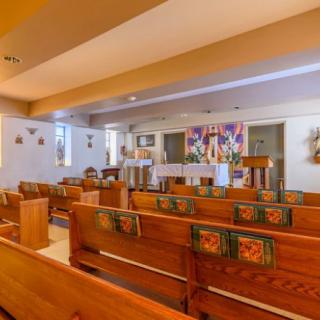 A small, decorated chapel interior with wooden pews and an altar.
