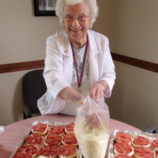 An elderly woman is smiling while preparing food in the kitchen.
