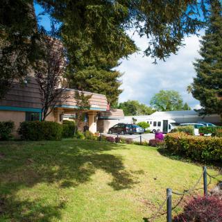 A scenic view of a building surrounded by trees and a well-maintained lawn, with cars parked nearby.
