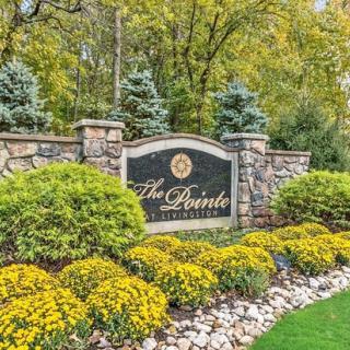 A landscaped entrance with a stone wall and sign reading 'The Pointe' surrounded by shrubs and flowers.