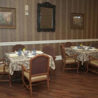 A dining room with several tables set for a meal, featuring tablecloths and elegant place settings, with artwork and a mirror on the walls.