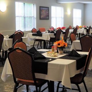 An empty dining room with neatly arranged tables and chairs, decorated with tablecloths and flower arrangements.