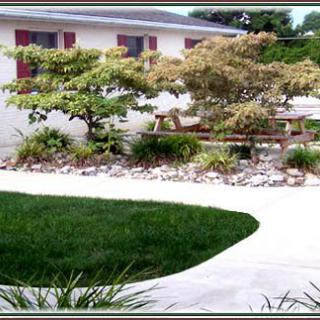 A beautifully maintained garden with a lush green lawn, various trees and shrubs, and a clean pathway leading around the area.