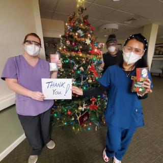 Healthcare workers express gratitude during the holiday season in front of a beautifully decorated Christmas tree.