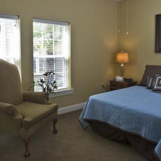 A cozy bedroom with a bed, armchair, and a lamp beside the window.