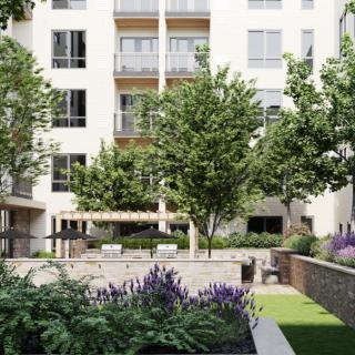 A modern apartment building with a well-maintained courtyard featuring lush greenery and outdoor seating.