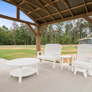 A cozy patio area with white furniture under a wooden pergola, overlooking lush greenery and trees.