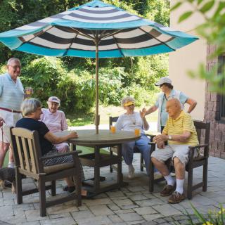 A group of seniors socializing outdoors on a patio under an umbrella.