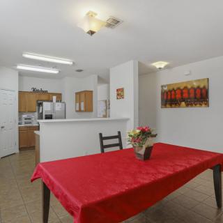 A cozy dining area with a red tablecloth and flowers, adjacent to a modern kitchen.