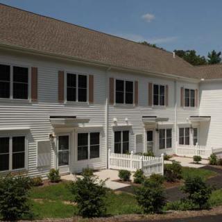 A white townhouse with multiple windows and landscaped surroundings in a suburban area.