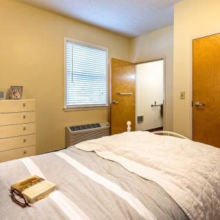 A cozy bedroom with a neatly made bed, a dresser, and an open door to an adjoining room.