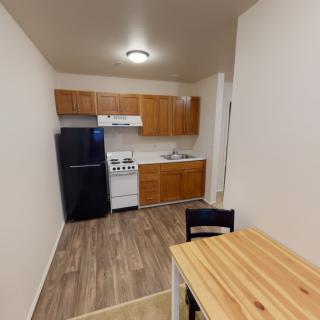 A compact apartment kitchen with wooden cabinets and a small dining area.