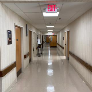 A hospital hallway with multiple doors and an exit sign visible at the end.