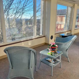 A cozy indoor seating area with two chairs and a table adorned with flowers, surrounded by large windows that let in plenty of natural light.