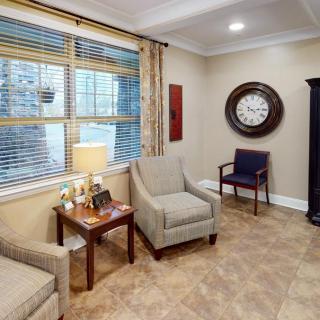 A cozy waiting room with comfortable seating, a large wall clock, and soft lighting from a table lamp.